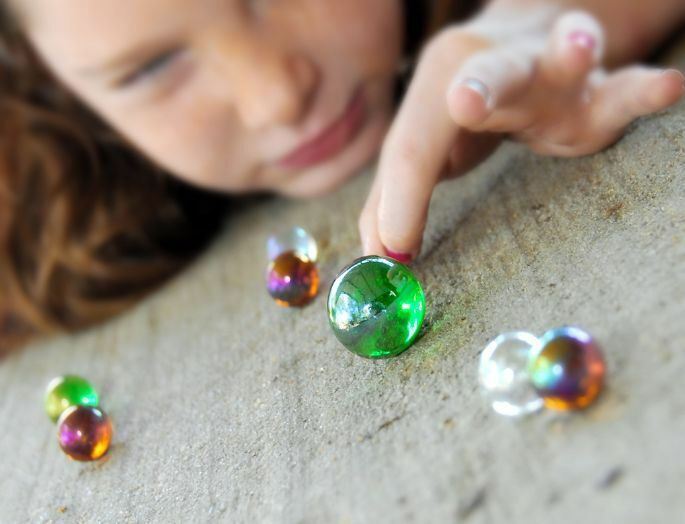 Juego tradicional canicas. Una niña juega a las canicas.