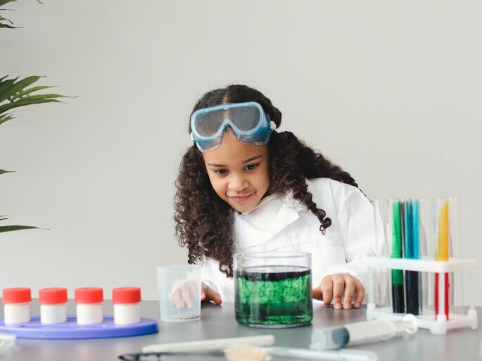 Una niña realizando un experimento con un líquido y tinte de color verde.