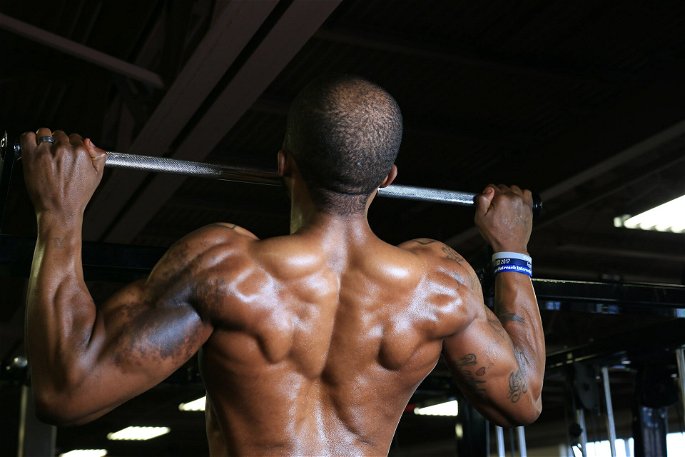 Un hombre afroamericano haciendo dominadas en el gimnasio para mejorar su resistencia muscular.