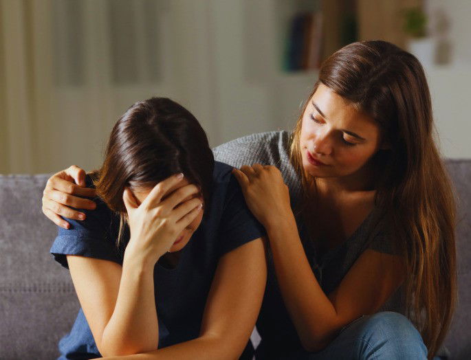 una chica consuela a su amiga que está llorando sentadas en un sofa