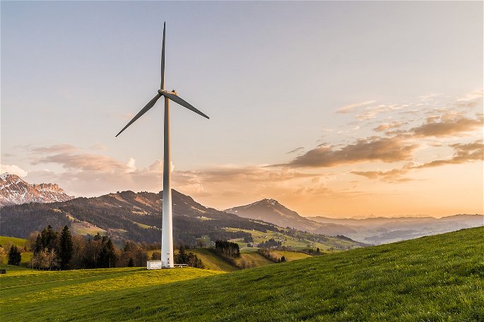 Turbina eólica en una zona verde y montañosa, en el atardecer