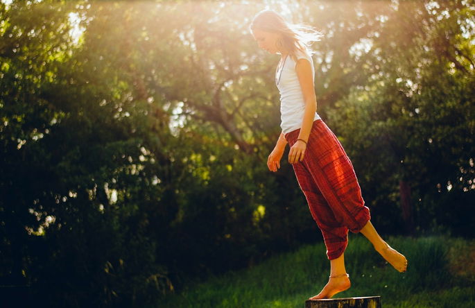 Una mujer equilibrándose sobre un pie encima de un tronco de árbol, poniendo a prueba su equilibrio estático.