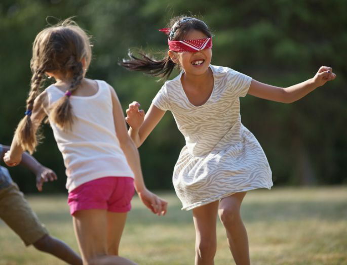 Juego tradicional gallinita ciega. Dos niñas juegan a la gallinita ciega. Una de ellas lleva los ojos vendados.