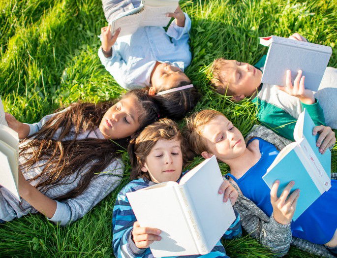 Grupo de niños leyendo sobre hierba verde