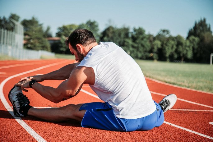 Un hombre realizando estiramientos músculos en una pista para mejorar su flexibilidad y calentar