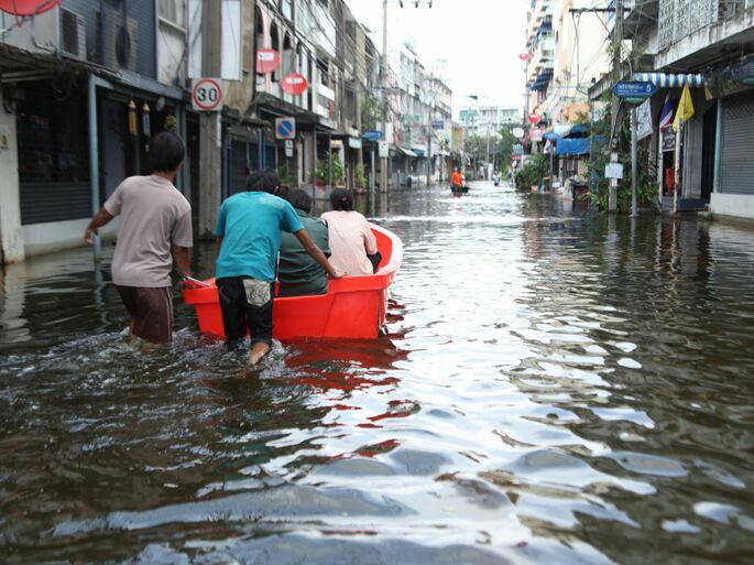 Dos jóvenes empujando un bote con tres personas en él a través de una carretera inundada de una ciudad.