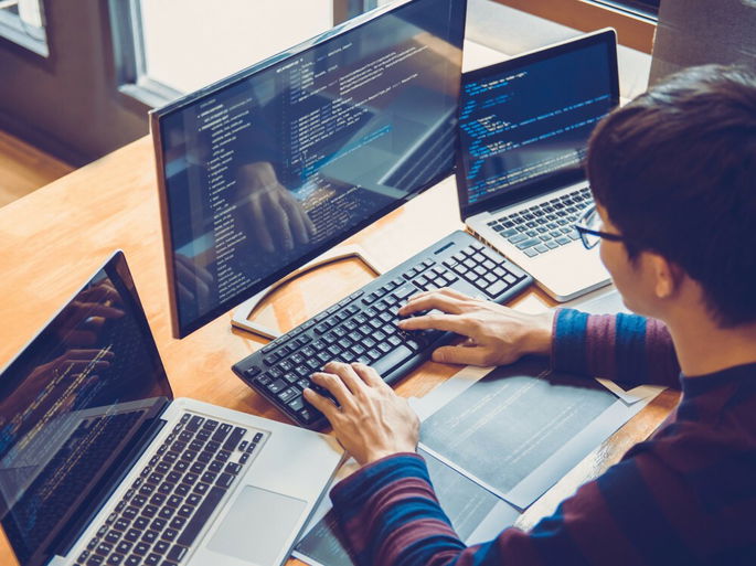 Un joven utilizando una computadora de escritorio y dos computadoras portátiles