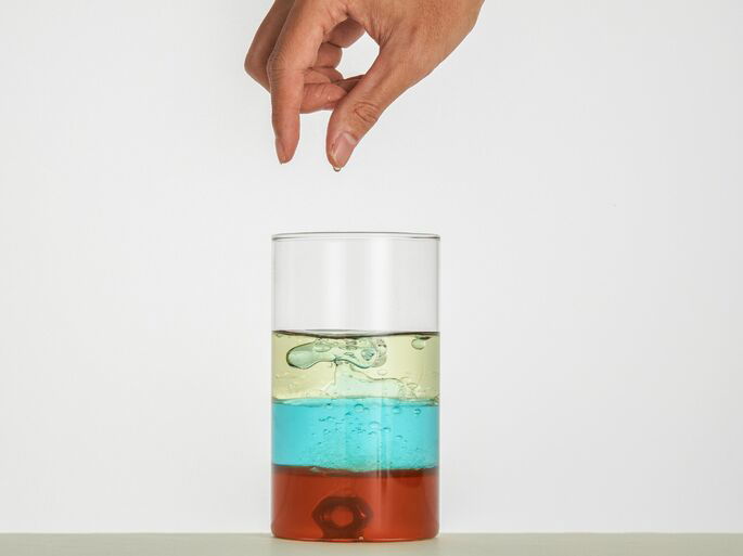 Mezcla de aceite, agua y otro líquido en un vaso de cristal.