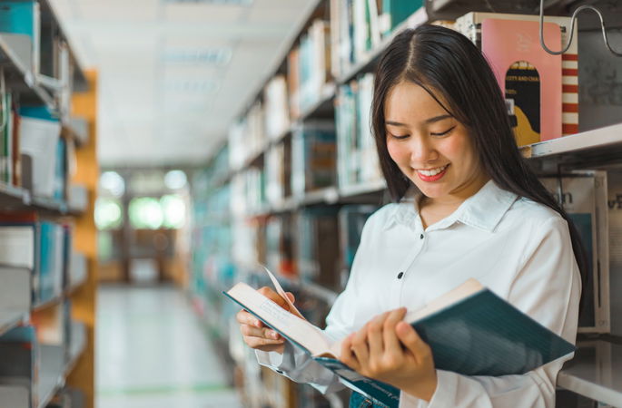 Mujer joven leyendo en biblioteca con estanterías