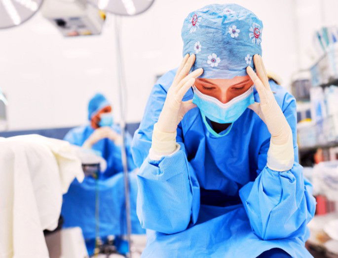 médico en quirófano con las manos en la cabeza y mirando al suelo