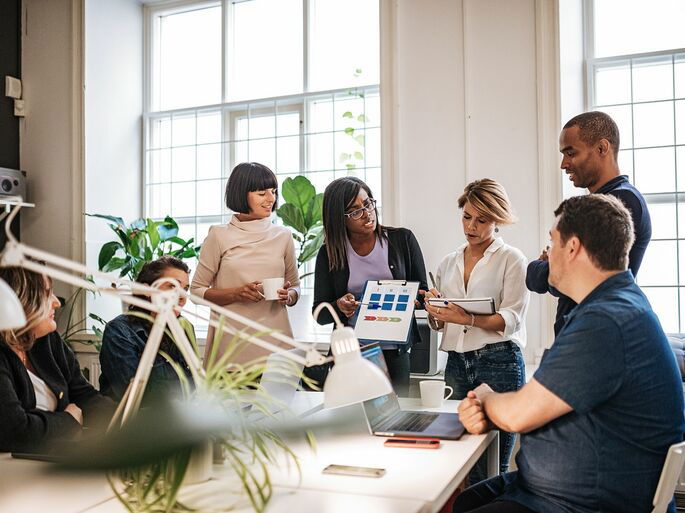 Cinco mujeres y dos hombres tomando decisiones en una oficina de trabajo.