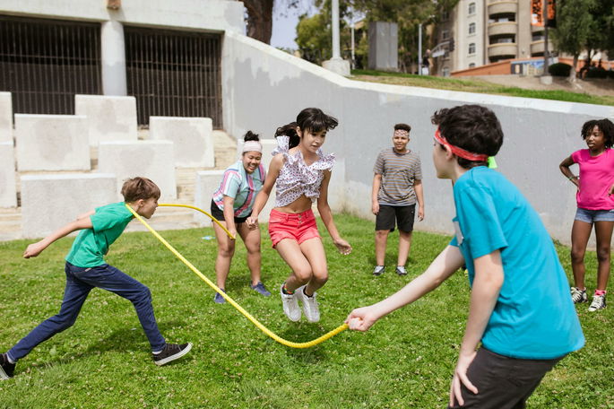 Niños jugando y saltando a la comba en un jardín.