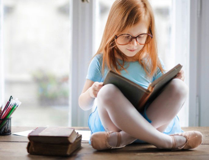 Niña sentada frente a la ventana leyendo un libro