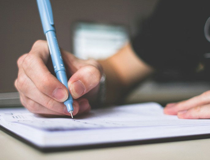 Muchacho sentado en una mesa, escribiendo en un cuaderno.