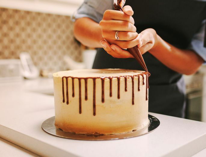 Repostero decorando un pastel con una manga pastelera llena de salsa de chocolate