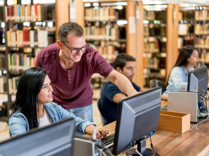 Un hombre y una mujer en una biblioteca, utilizando una computadora para buscar información.