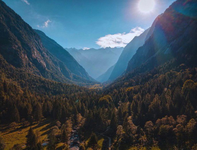 Valle entre dos montañas boscosas y suelo con hierba y vegetación