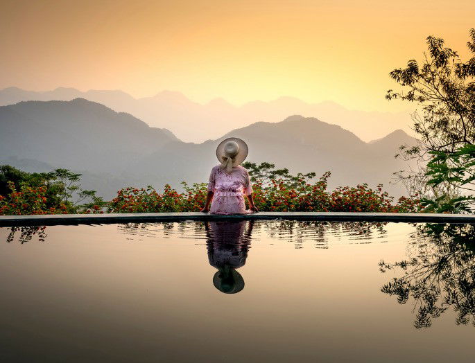 fotografía de una mujer de vacaciones, sentada delante de una piscina enfrente de un bello paisaje natural