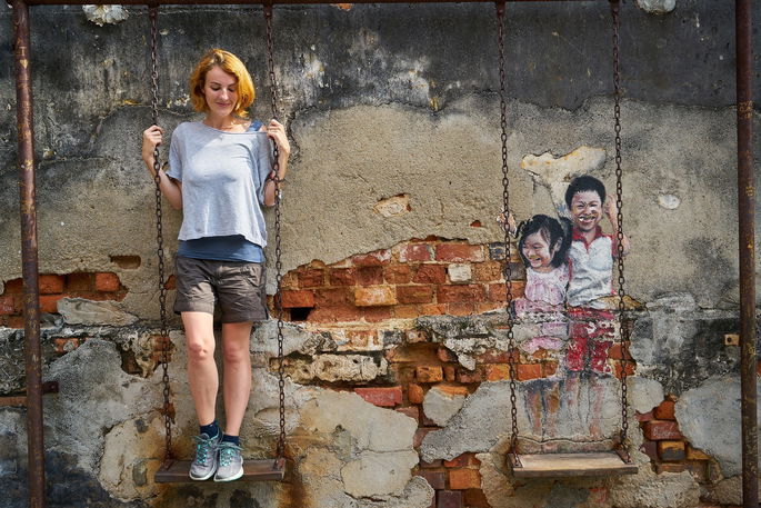 Joven interactúa con una instalación urbana de arte callejero en Georgetown, Malasia.